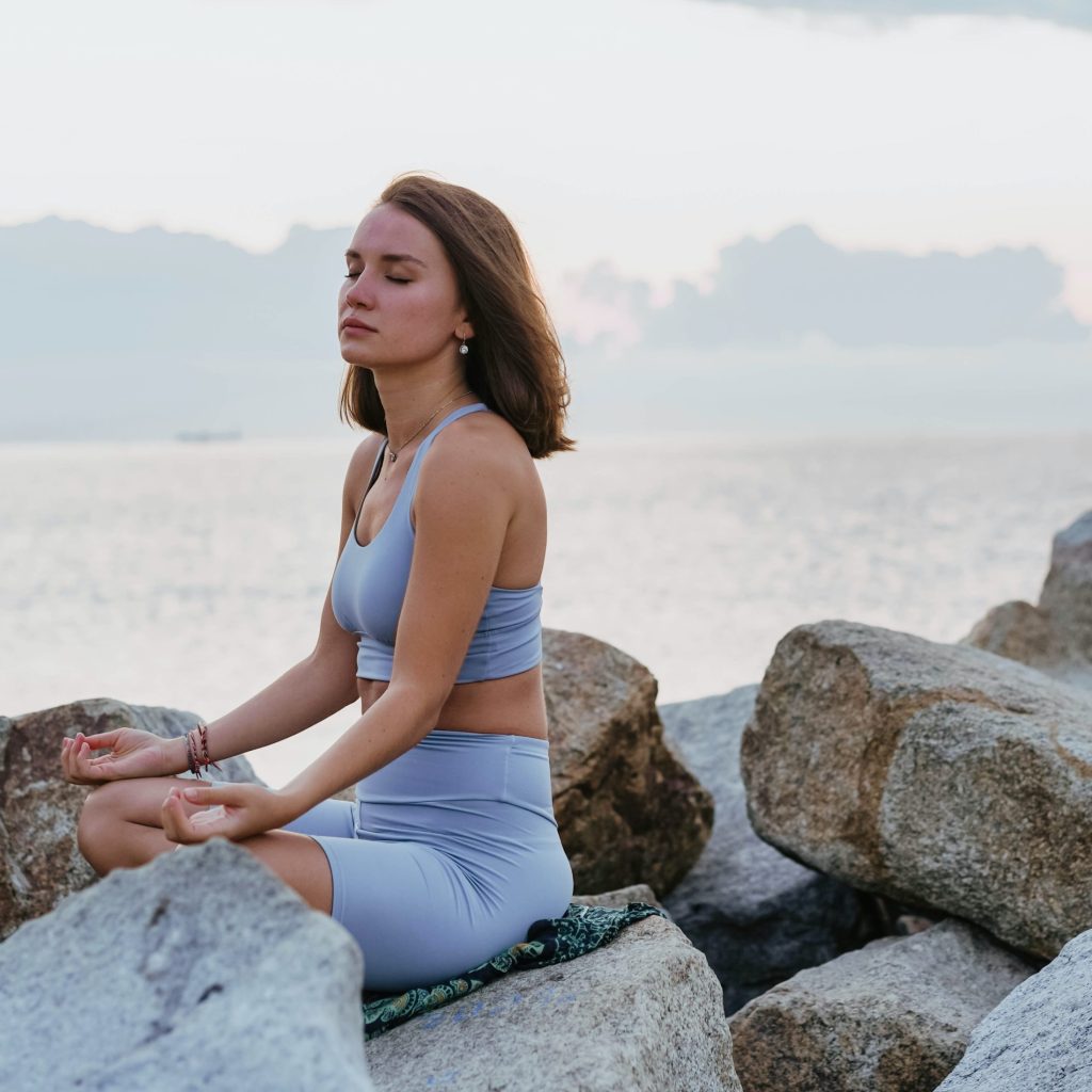 A girl meditating on the rocks by the ocean